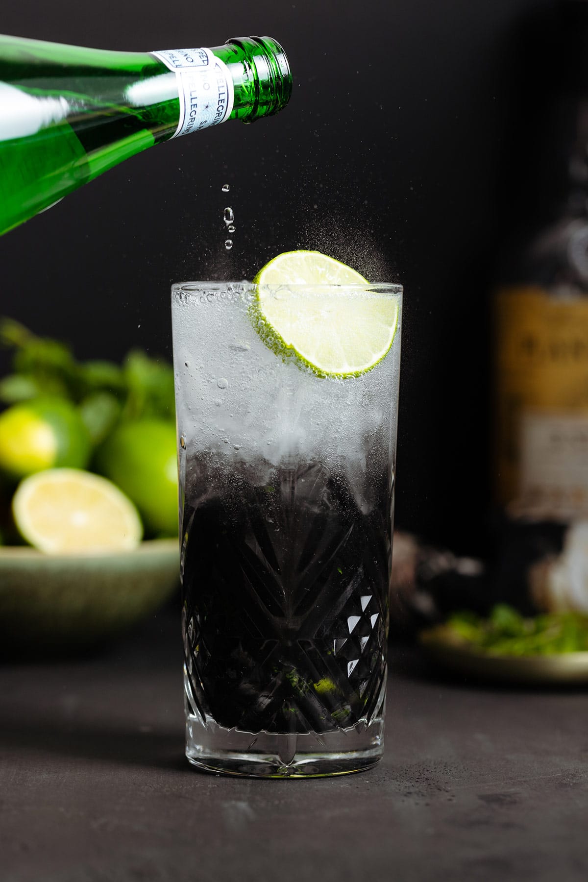 Black mojito with sparkling water being poured on top creating an ombre effect.
