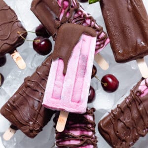 Pink cherry popsicles partially covered with dark chocolate on a white serving plate with ice.
