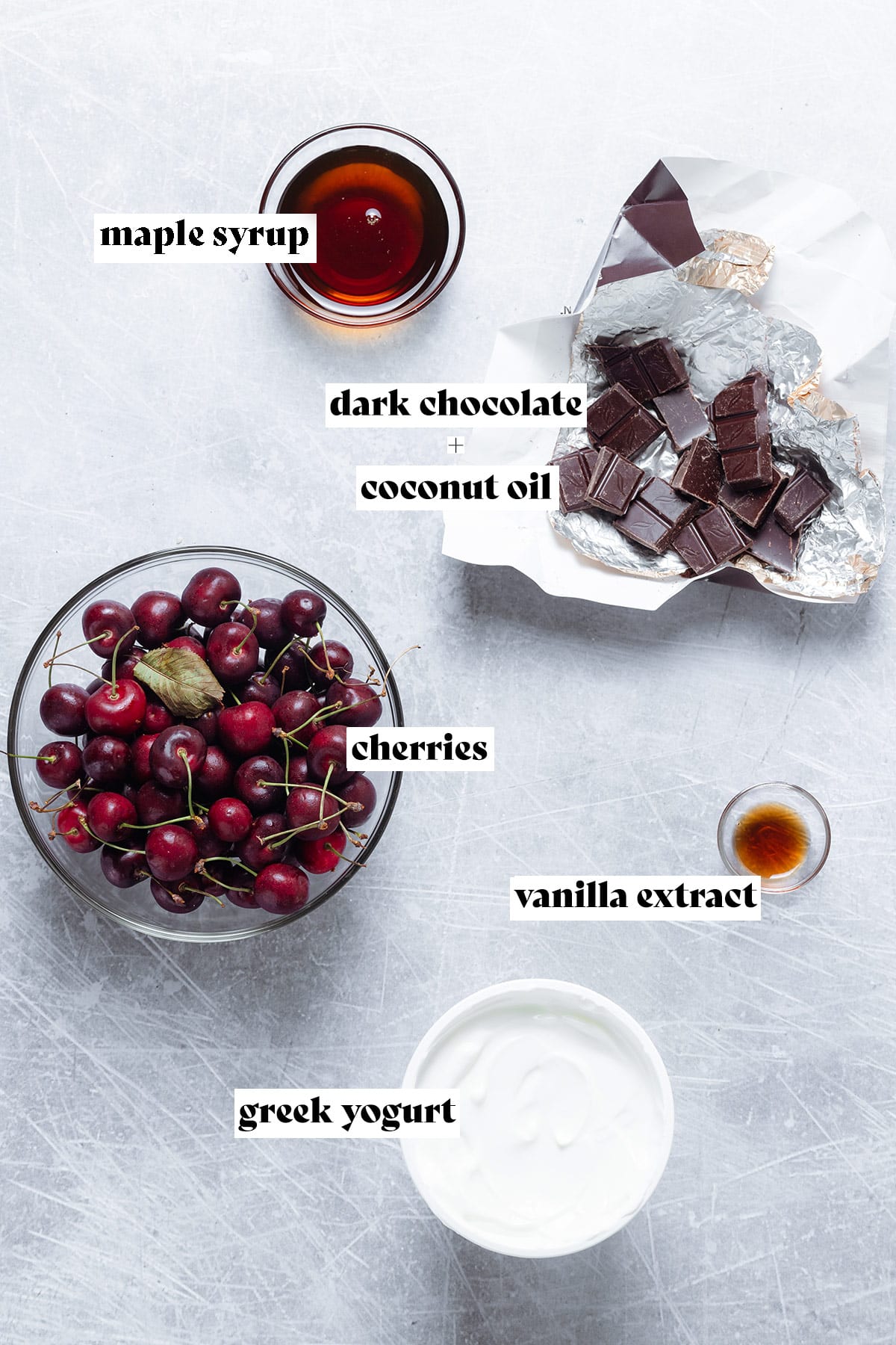 Ingredients for popsicles like cherries, yogurt, and chocolate laid out on a light grey background.