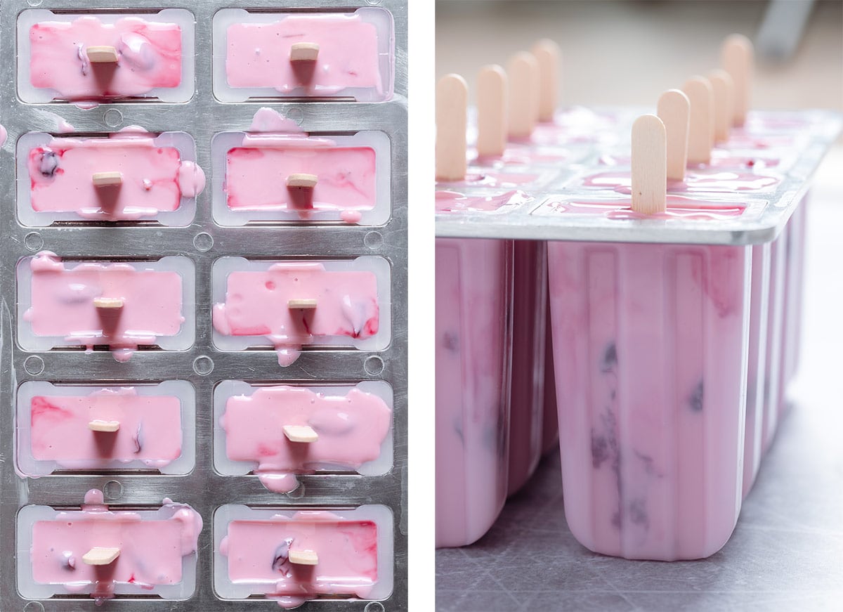 Popsicle molds filled with pink yogurt, cherries, and popsicle sticks.