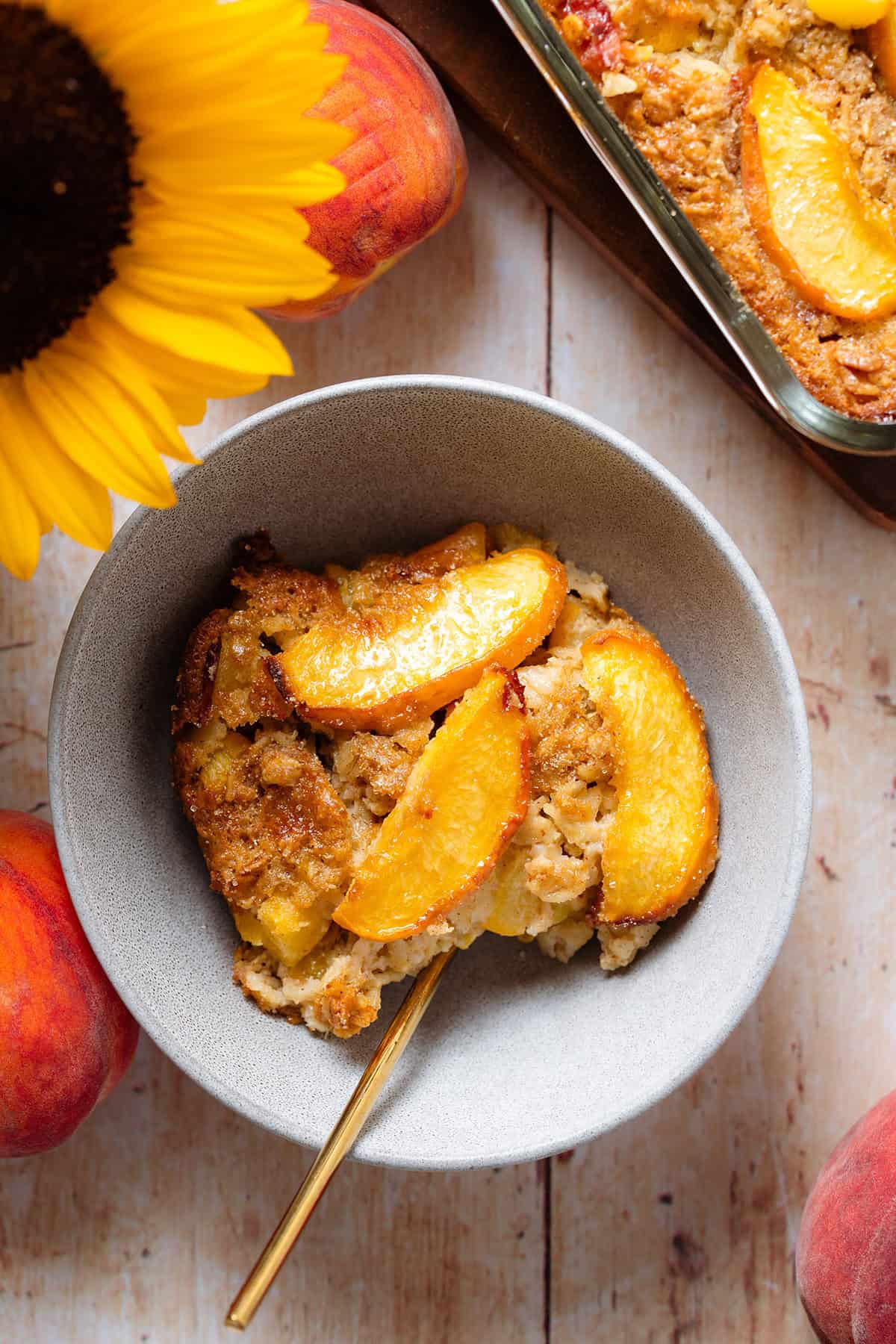 Peach baked oatmeal in a grey bowl topped with peaches and more baked oatmeal on the right.