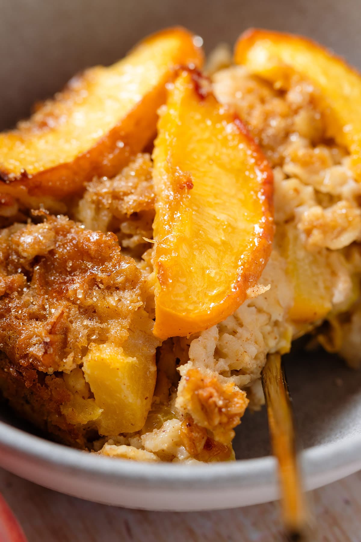 A close up of baked oatmeal with peaches in a grey bowl.