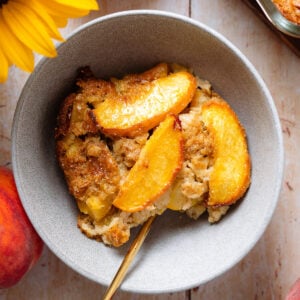 Peach baked oatmeal in a grey bowl topped with peaches and more baked oatmeal on the right.