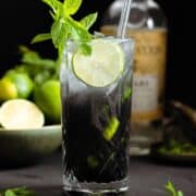 Black mojito with sparkling water on top creating an ombre effect in a tall glass garnished with a slice of lime and fresh mint.