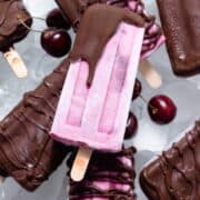 Pink cherry popsicles partially covered with dark chocolate on a white serving plate with ice.