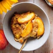 Peach baked oatmeal in a grey bowl topped with peaches and more baked oatmeal on the right.