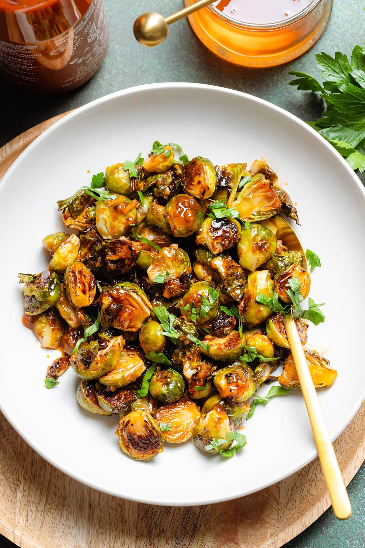 Charred saucy brussels sprouts in a white bowl with a gold serving spoon on the right.