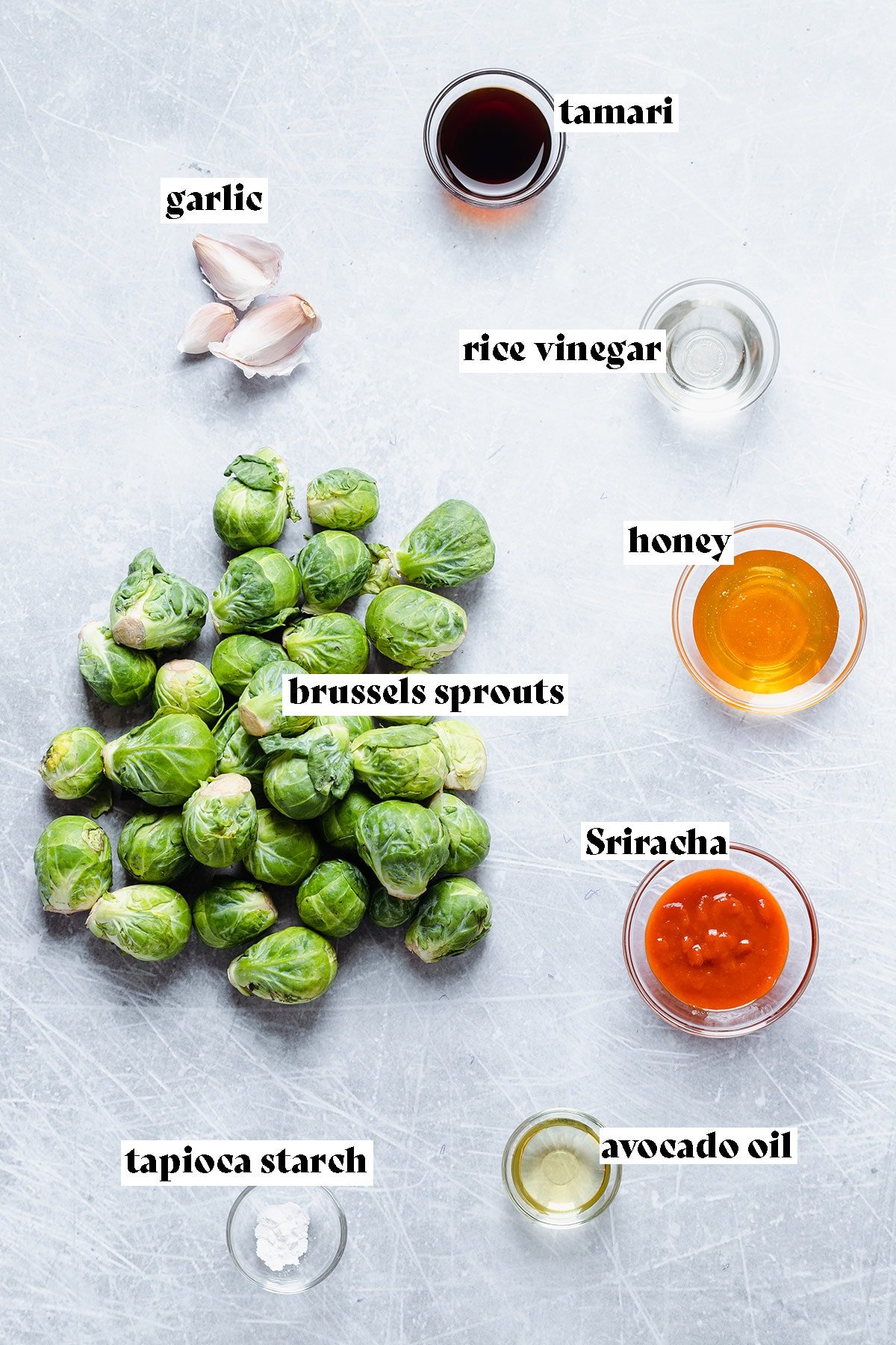 Brussels Sprouts, sriracha, honey, and other ingredients on a grey background.