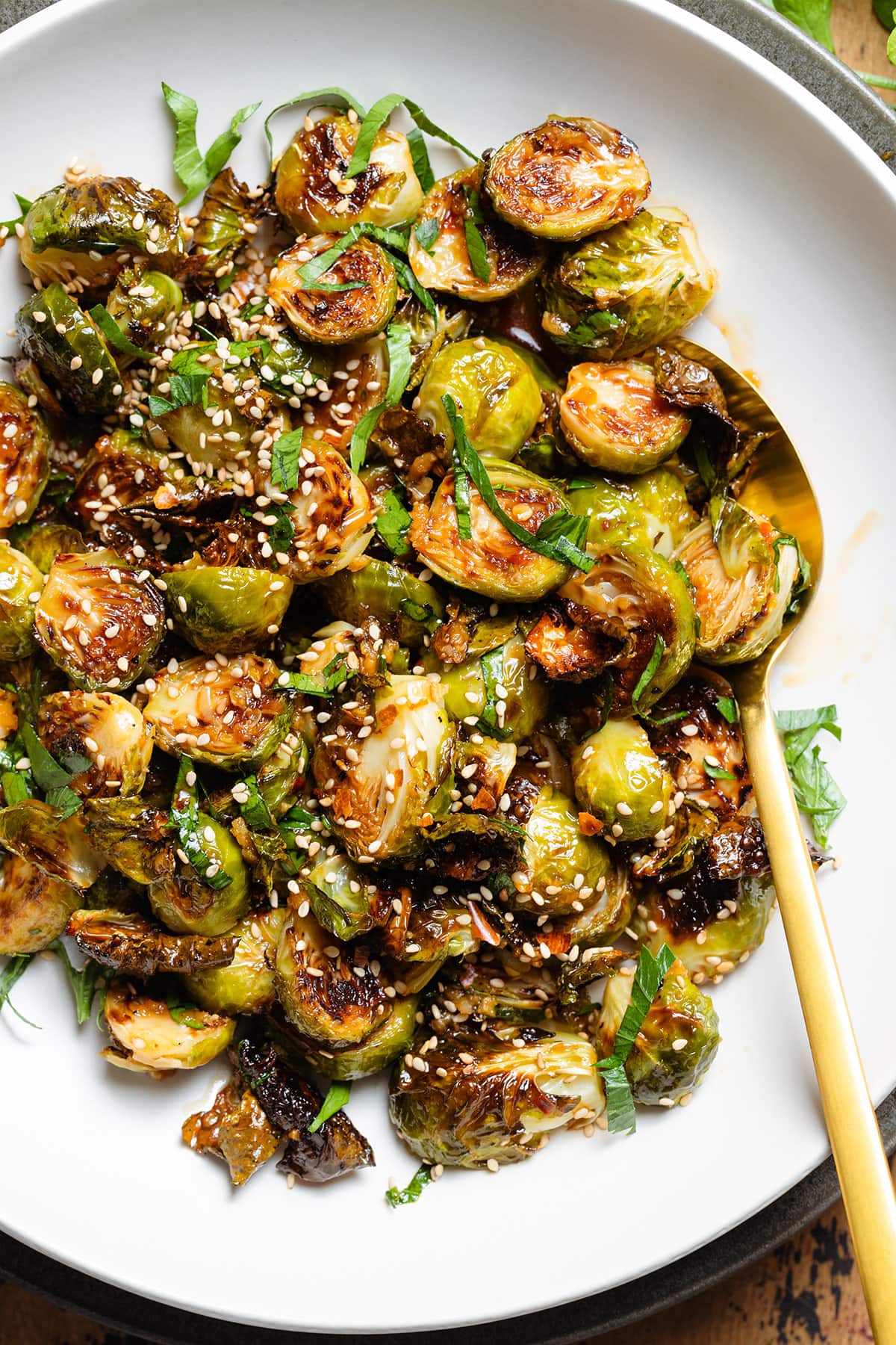 A white bowl with roasted brussels sprouts topped with fresh parsley and sesame seeds.