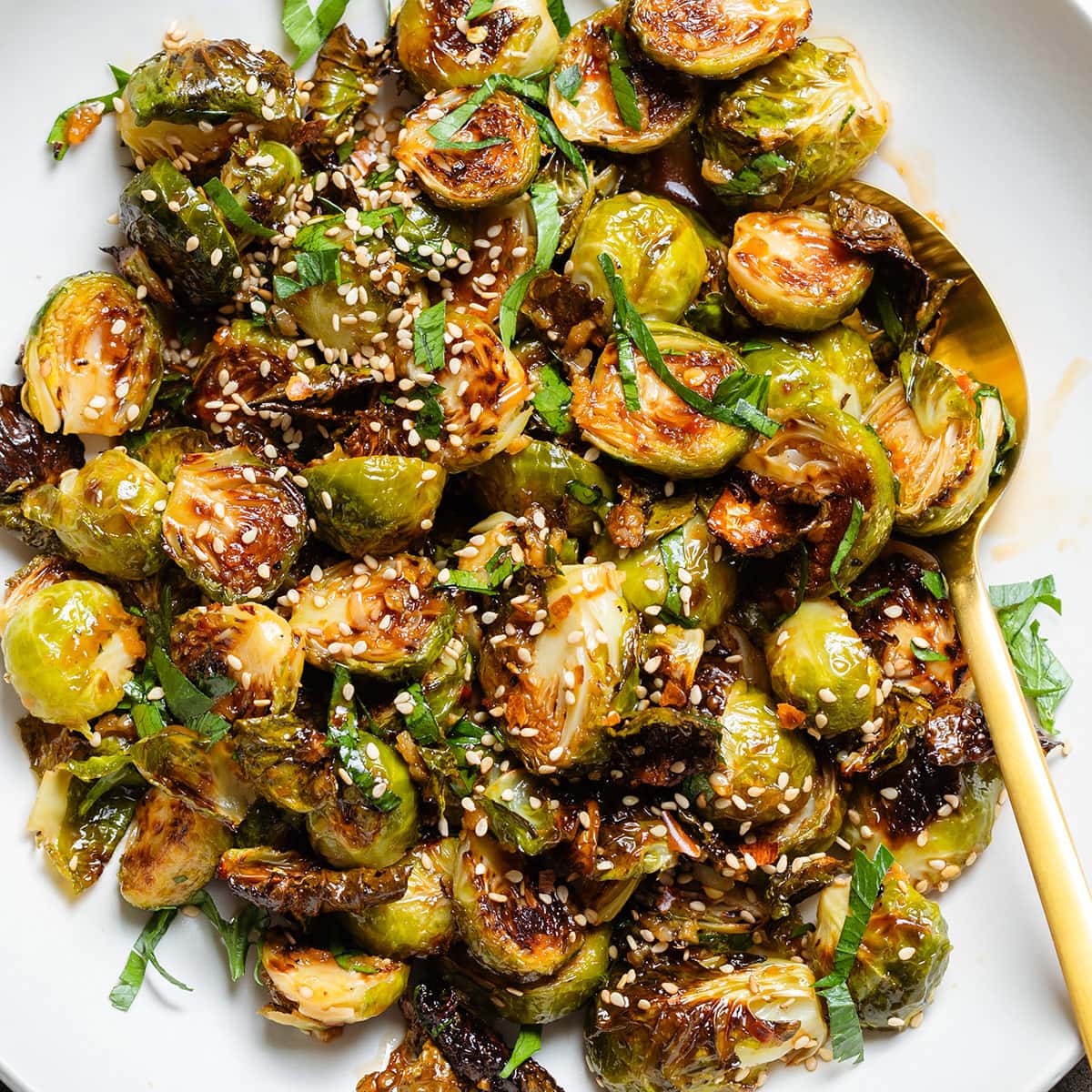A white bowl with roasted brussels sprouts topped with fresh parsley and sesame seeds.