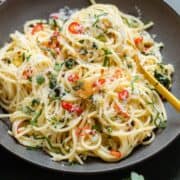 Spaghetti with parsley and chili peppers in a black bowl with a gold fork.