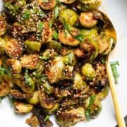 A white bowl with roasted brussels sprouts topped with fresh parsley and sesame seeds.