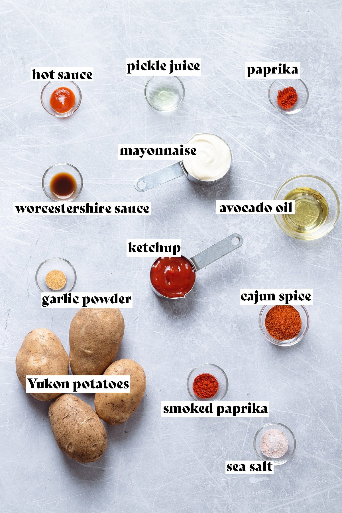 Potatoes, mayonnaise, ketchup, and other ingredients laid out on a grey background.