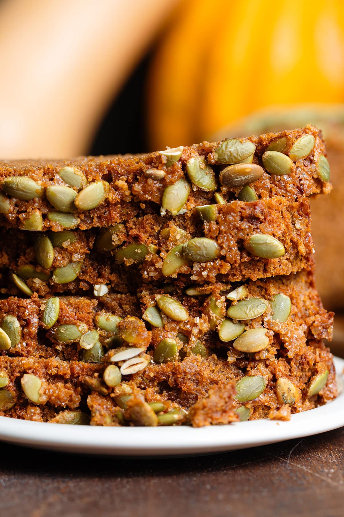 Slices of pumpkin bread with pumpkin seeds stacked up on a small white plate.