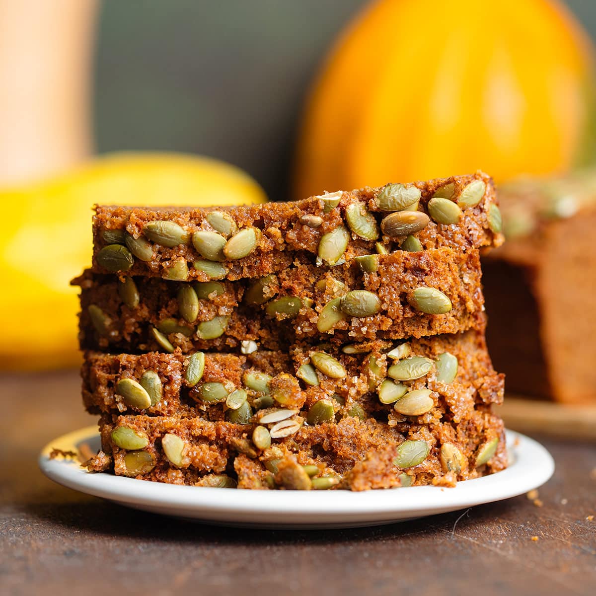 Slices of pumpkin bread with pumpkin seeds stacked up on a small white plate.