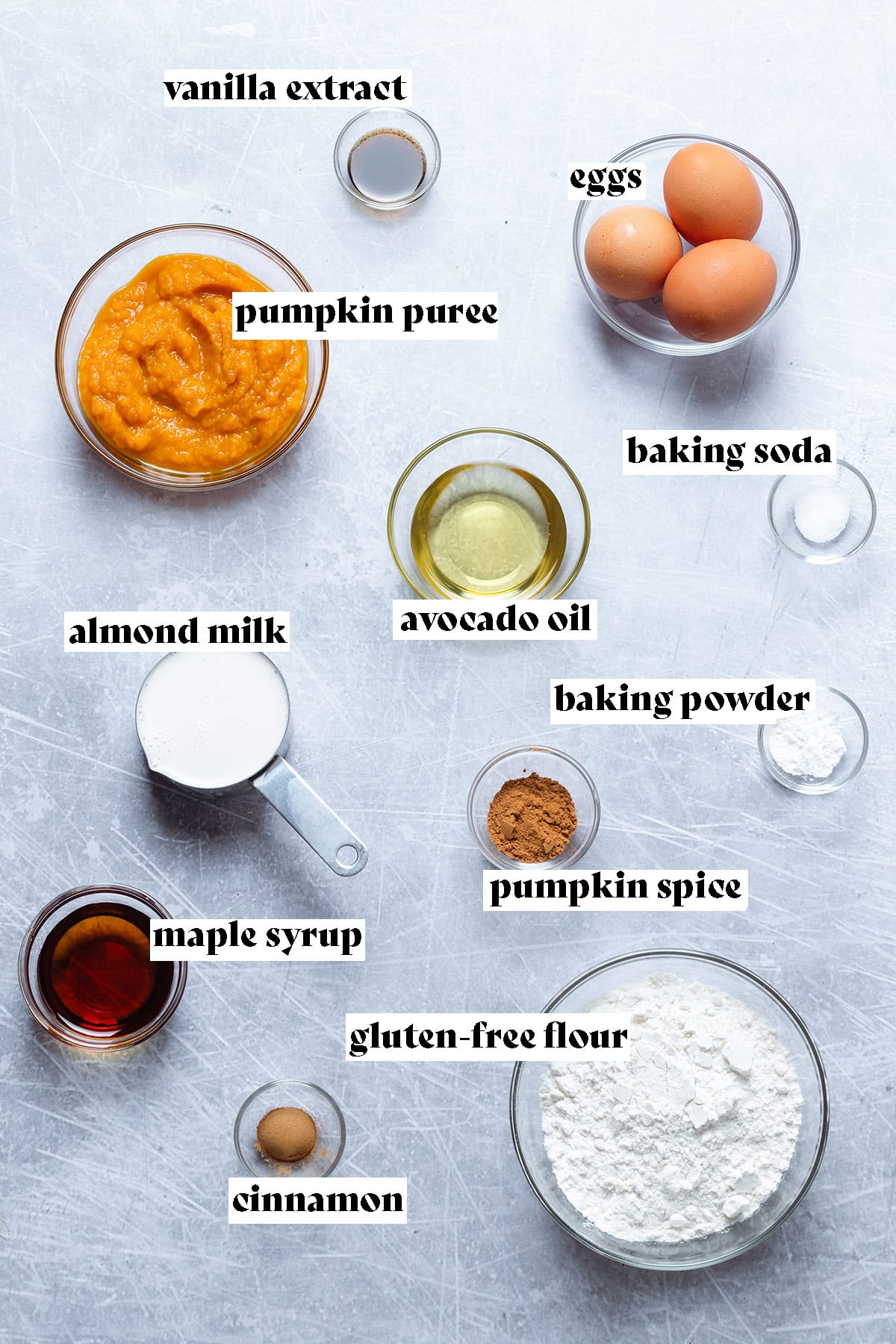 Ingredients like pumpkin puree, flour, milk, and eggs laid out on a grey background.