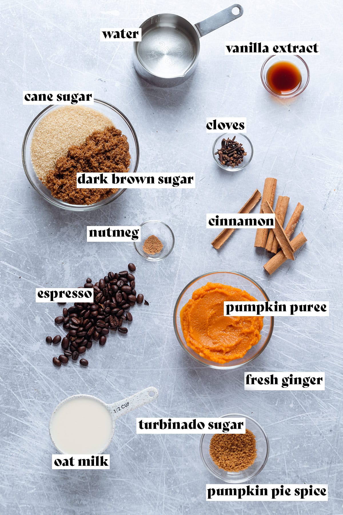 Pumpkin puree, sugar, cinnamon sticks, and other ingredients laid out on a grey background.