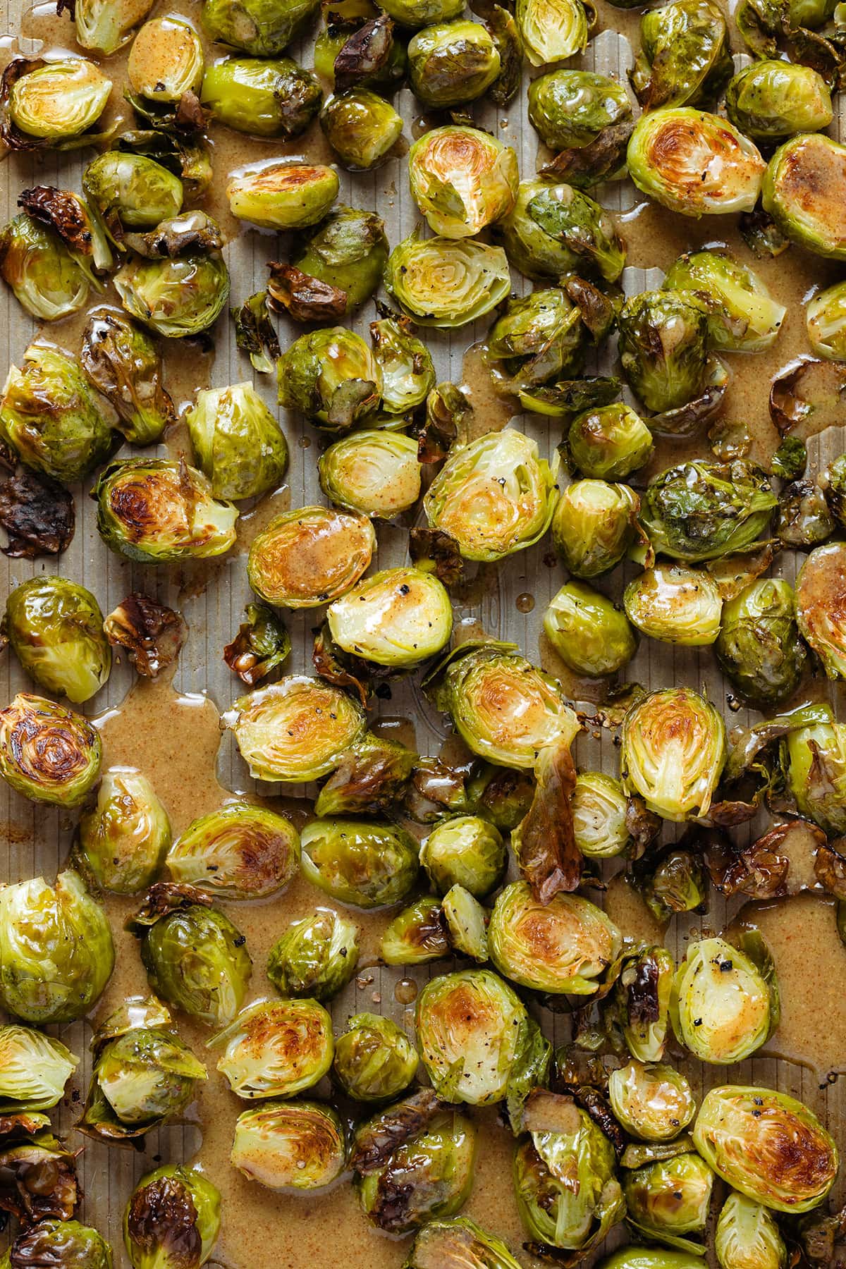 Roasted brussels sprouts on a baking sheet drizzled with a maple mustard vinaigrette.