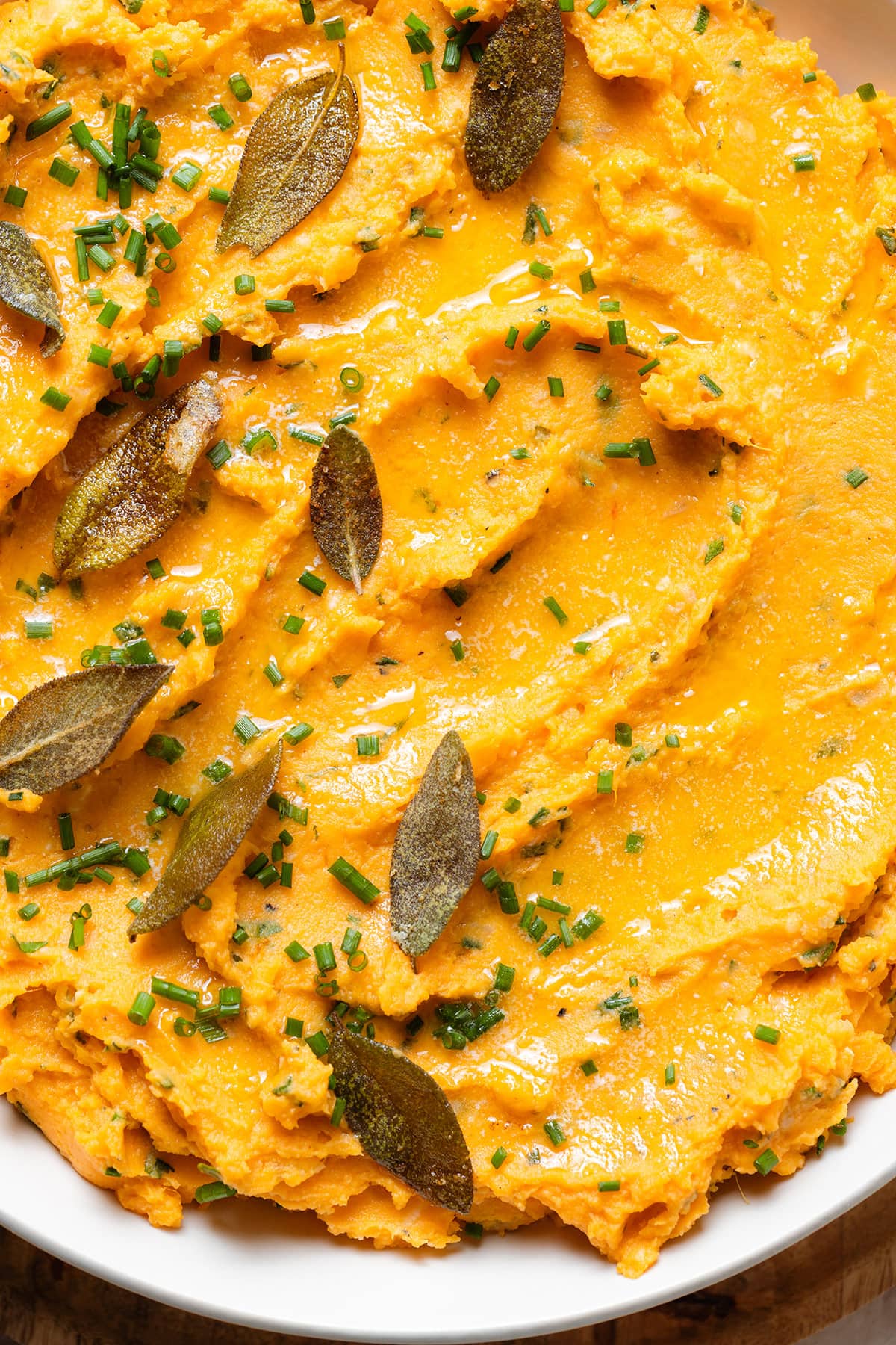 Mashed sweet potatoes in a white bowl topped with fried sage leaves and chives.