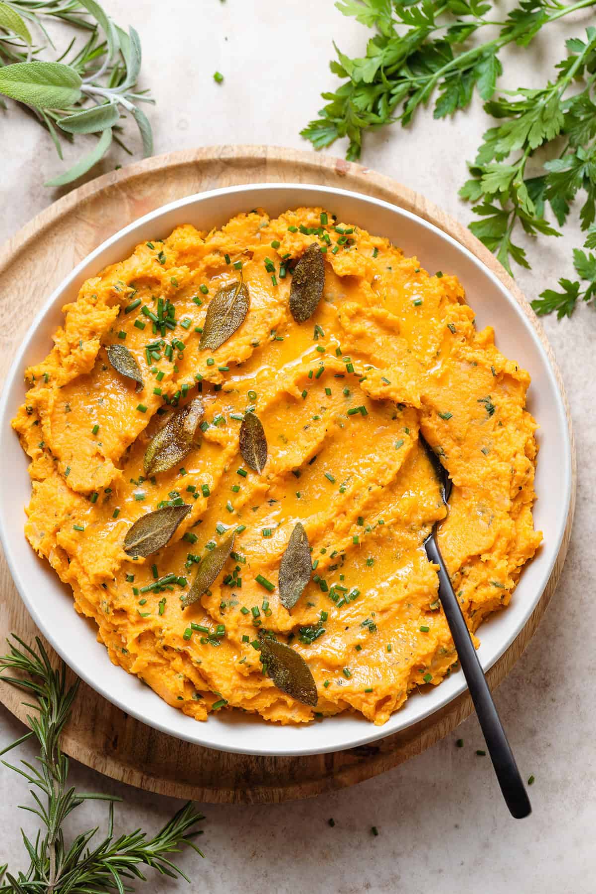 Mashed sweet potatoes in a white bowl topped with fried sage leaves and chives.