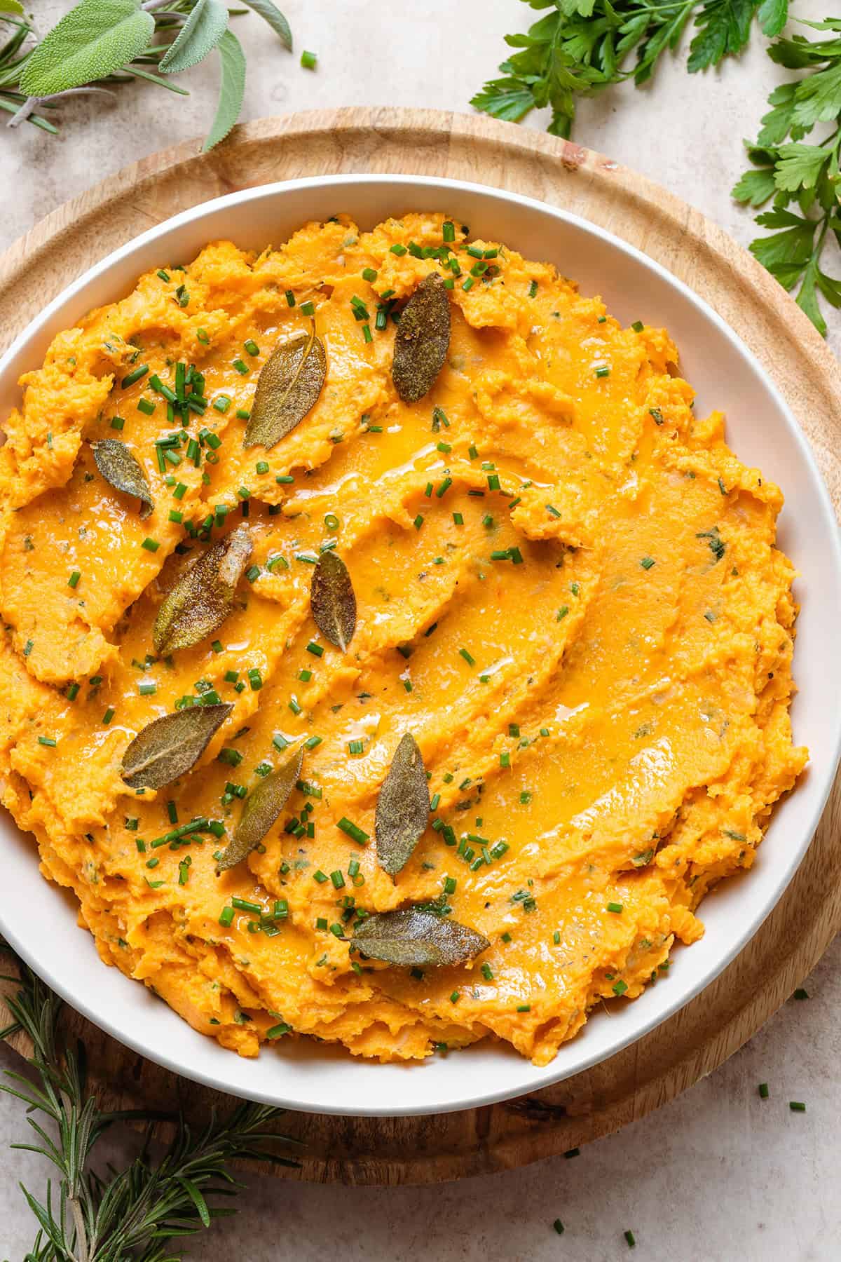 Mashed sweet potatoes in a white bowl topped with fried sage leaves and chives.