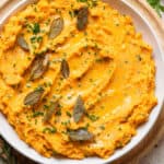 Mashed sweet potatoes in a white bowl topped with fried sage leaves and chives.