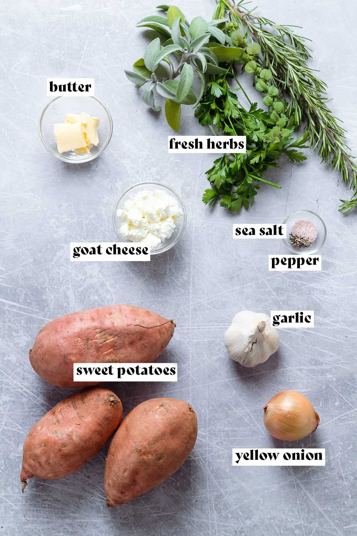 Sweet potatoes, garlic, yellow onion, and other ingredients laid out on a grey background.