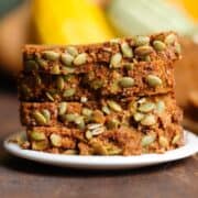 Slices of pumpkin bread with pumpkin seeds stacked up on a small white plate.