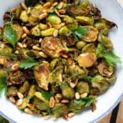 Charred brussels sprouts in a white bowl with a blue edge topped with a mustard vinaigrette, fresh parsley, and toasted pine nuts.