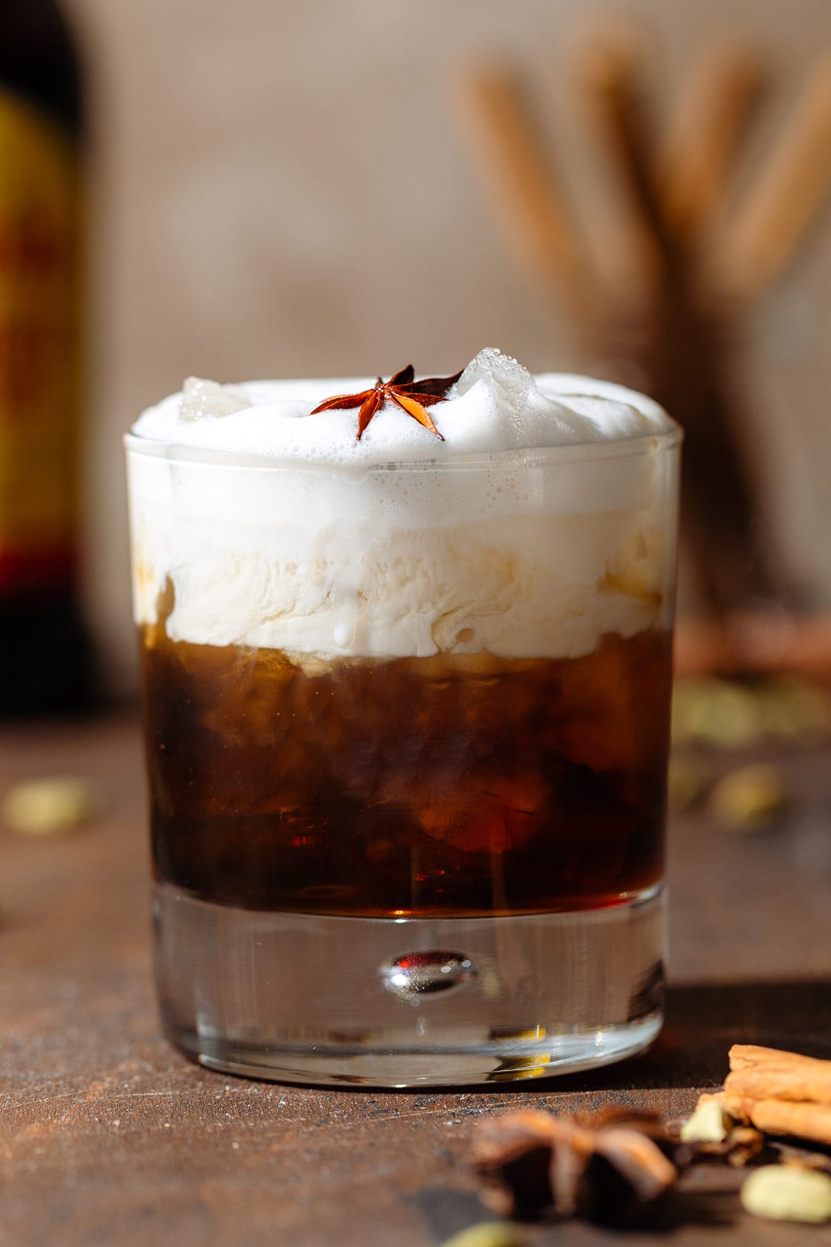 White Russian cocktail in a double old fashioned glass garnished with star anise on a wooden backdrop.