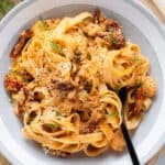 Fettuccine with creamy sundried tomato sauce and canned salmon in a low grey bowl topped with fresh dill and parmesan.