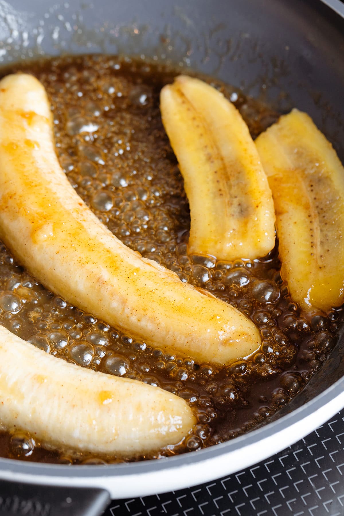 Bananas cooking with butter and maple syrup in a skillet.