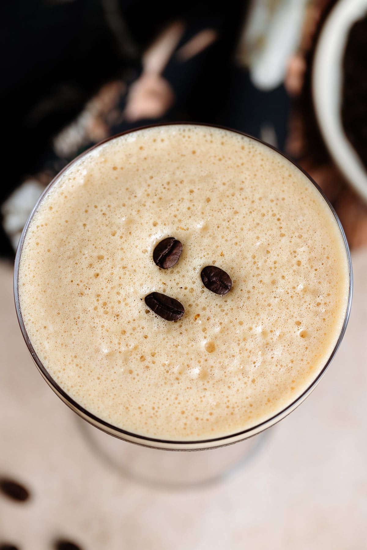 An espresso martini shot from above showing lots of coffee foam garnished with three coffee beans.