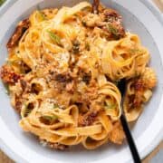 Fettuccine with creamy sundried tomato sauce and canned salmon in a low grey bowl topped with fresh dill and parmesan with a black fork on the right.