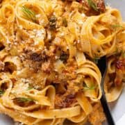 Fettuccine with creamy sundried tomato sauce and canned salmon in a low grey bowl topped with fresh dill and parmesan with a black fork on the right.