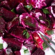 Beet salad with dollops of Greek yogurt and fresh herbs on a white serving platter with two serving spoons.