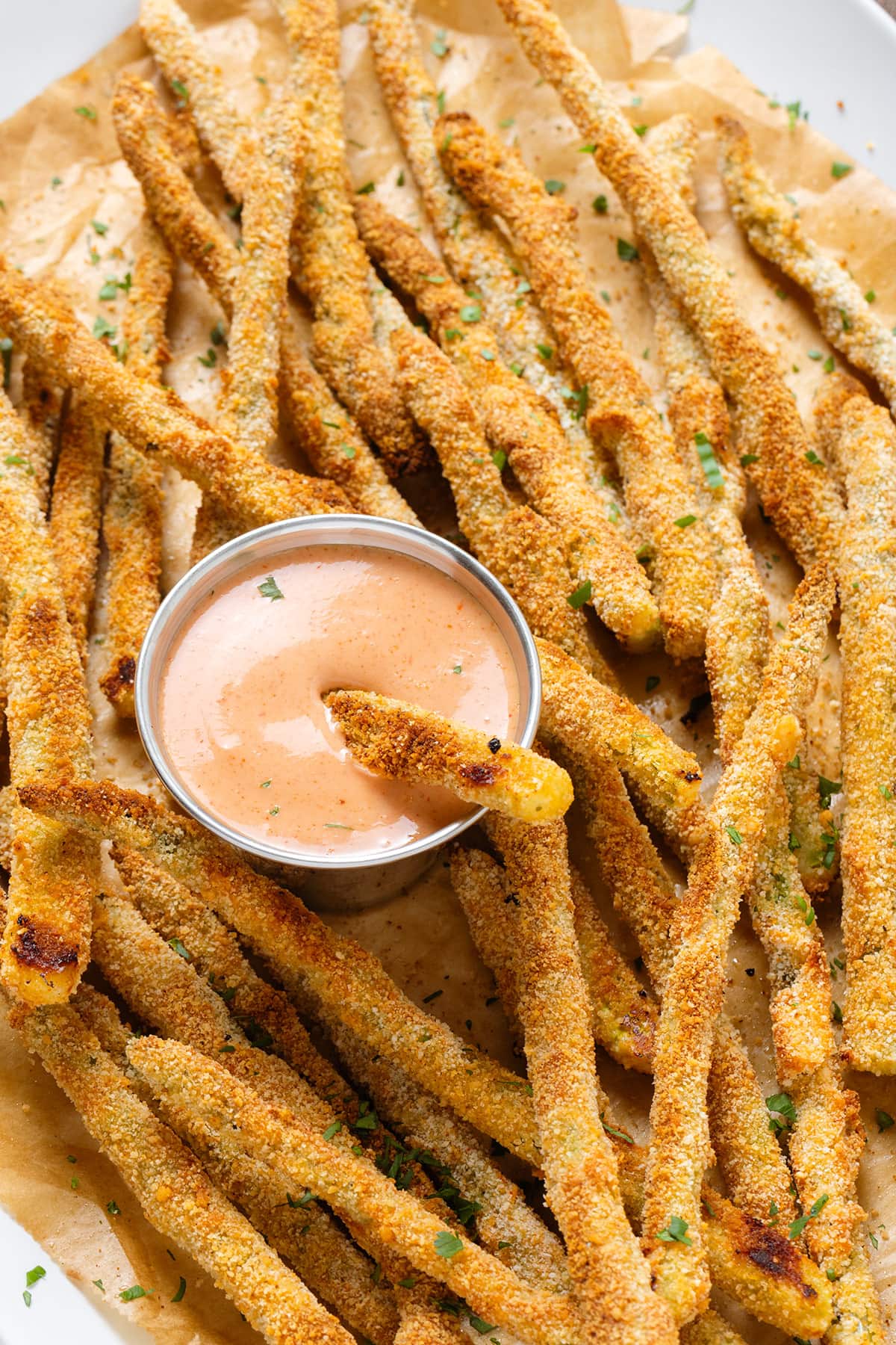 Crispy asparagus fries sprinkled with fresh parsley, served with house sauce that has one fry dipped into it.