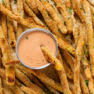 Crispy asparagus fries sprinkled with fresh parsley, served with house sauce that has one fry dipped into it.