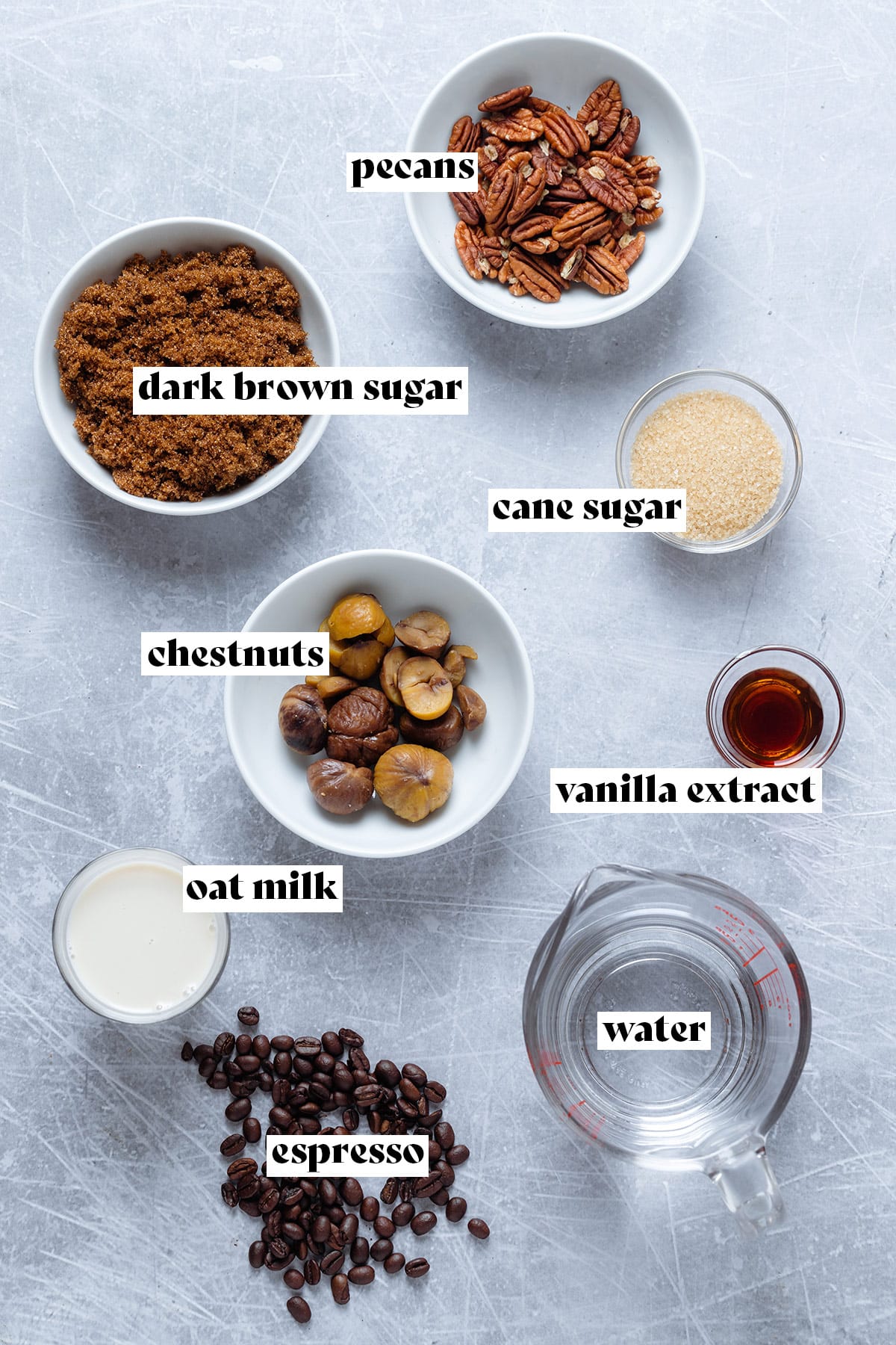 Ingredients like brown sugar, chestnuts, pecans, and water laid out on a grey background.