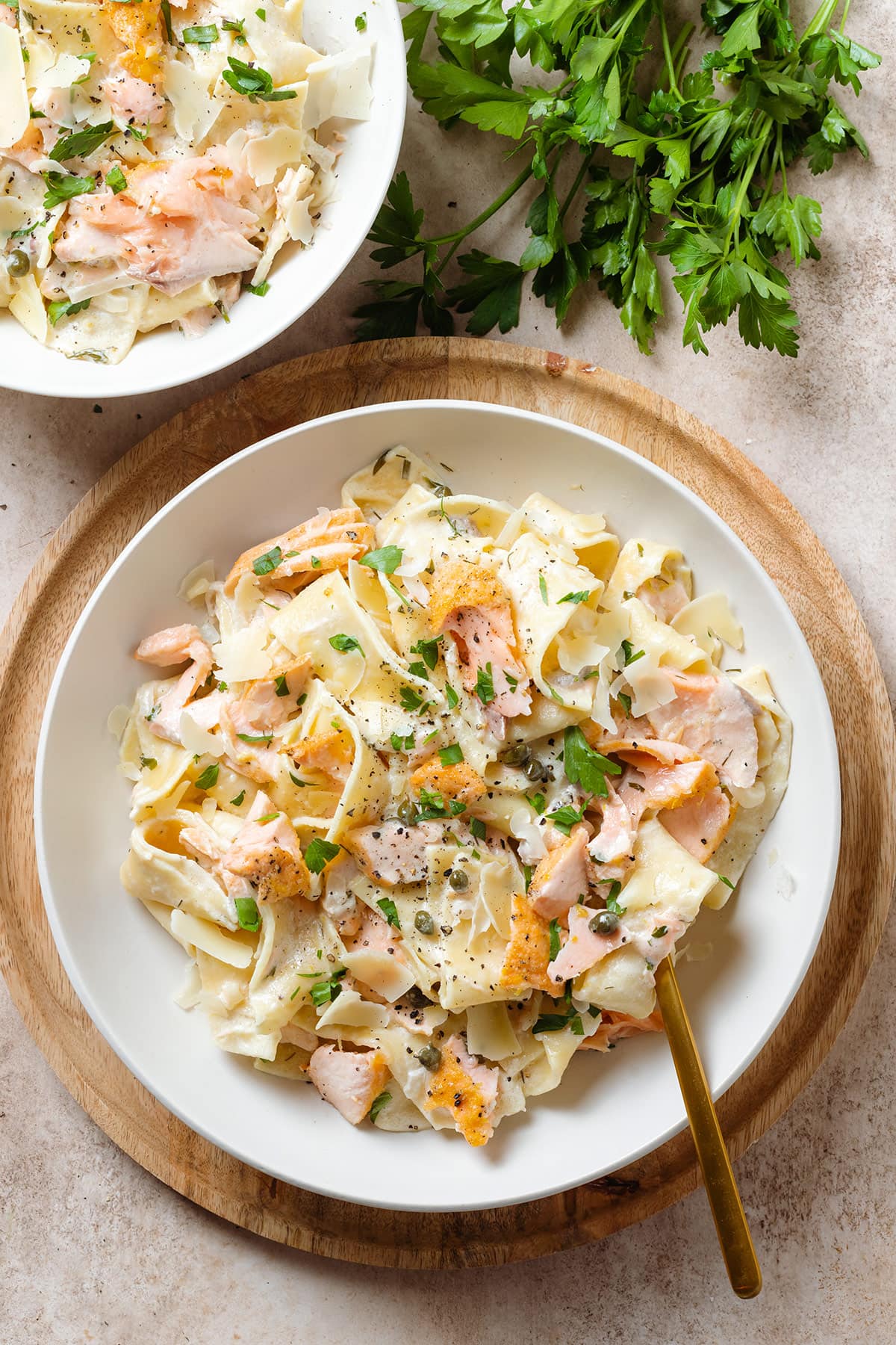 Pappardelle with roasted salmon, creamy white sauce, black pepper, and fresh herbs on a white plate.