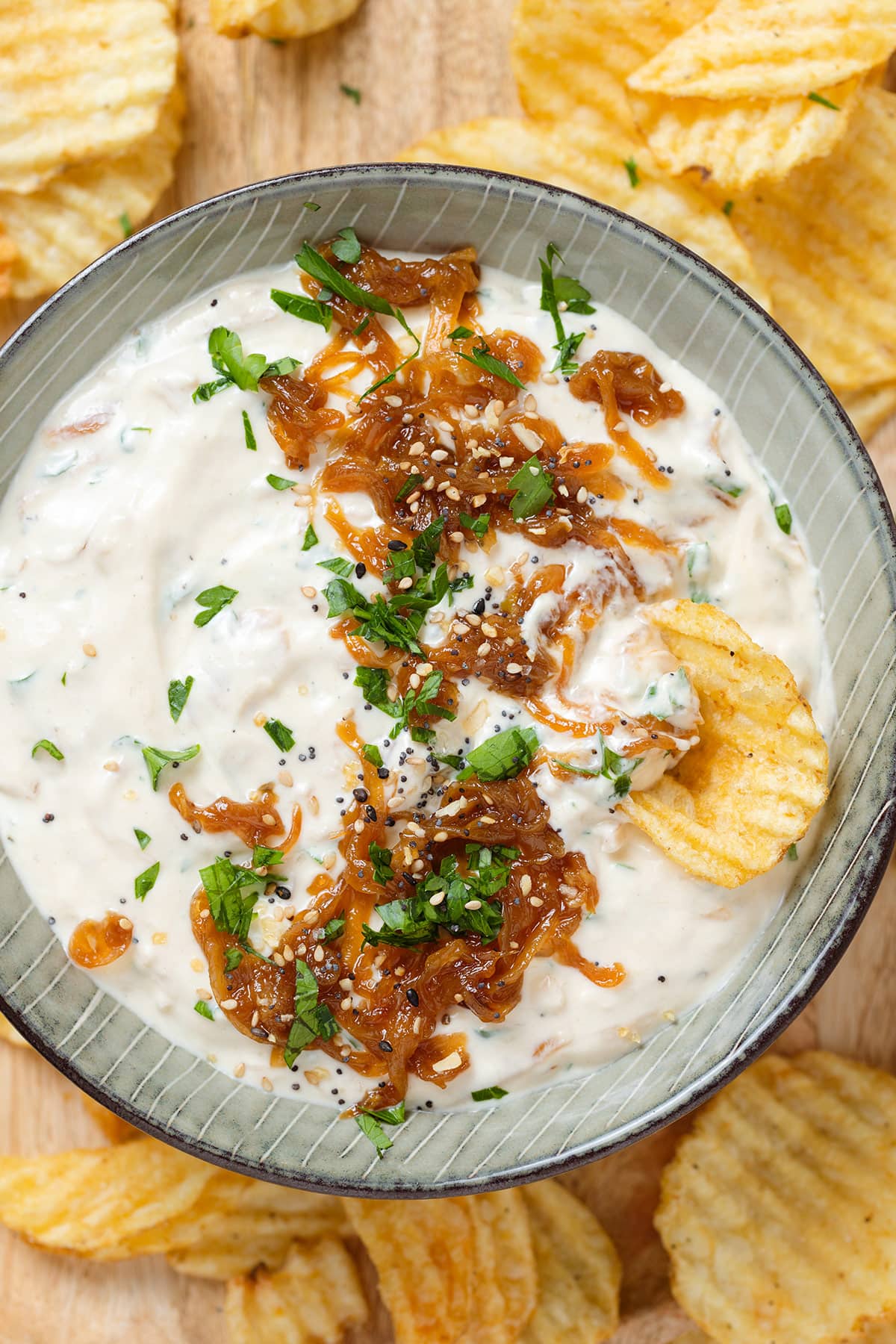 Onion dip garnished with caramelized onions in a stripped green bowl with crinkle cut chips all around the bowl.