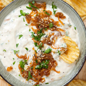 Onion dip garnished with caramelized onions in a stripped green bowl with crinkle cut chips all around the bowl.