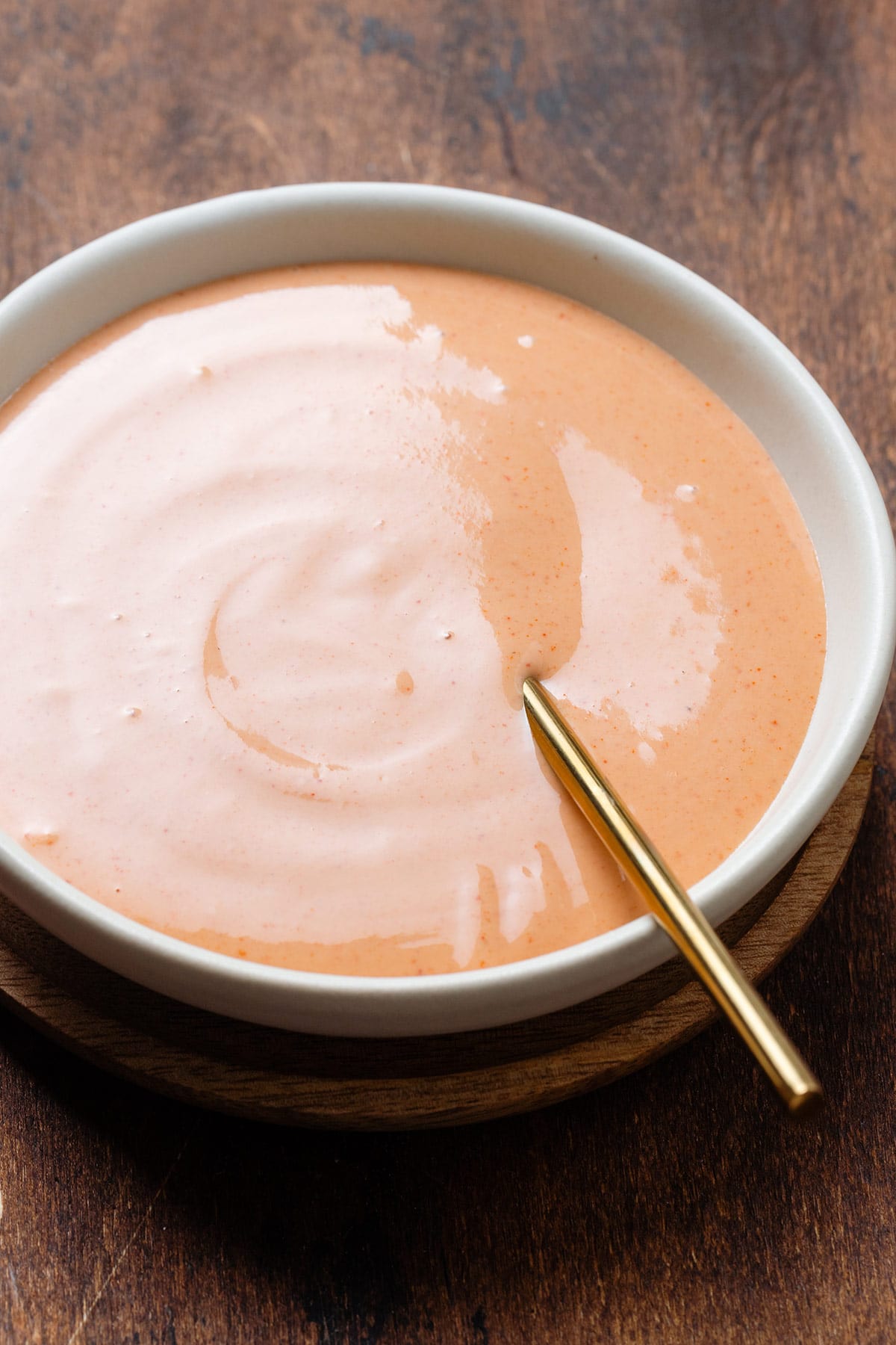 Creamy orange-colored house sauce in white bowl with a gold spoon on a dark wooden background.