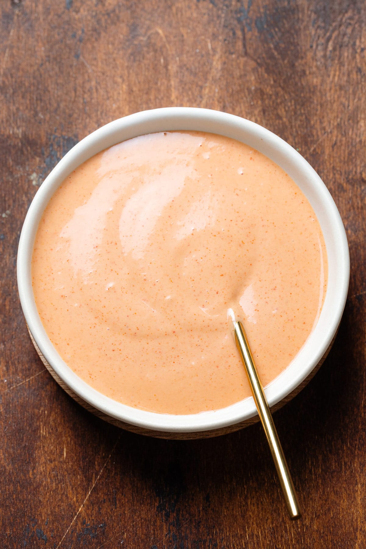 Creamy orange-colored house sauce in white bowl with a gold spoon on a dark wooden background.