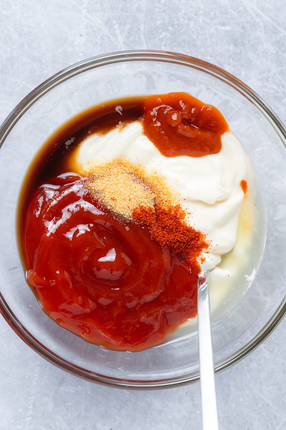 A glass bowl with ketchup, mayonnaise, and spices.