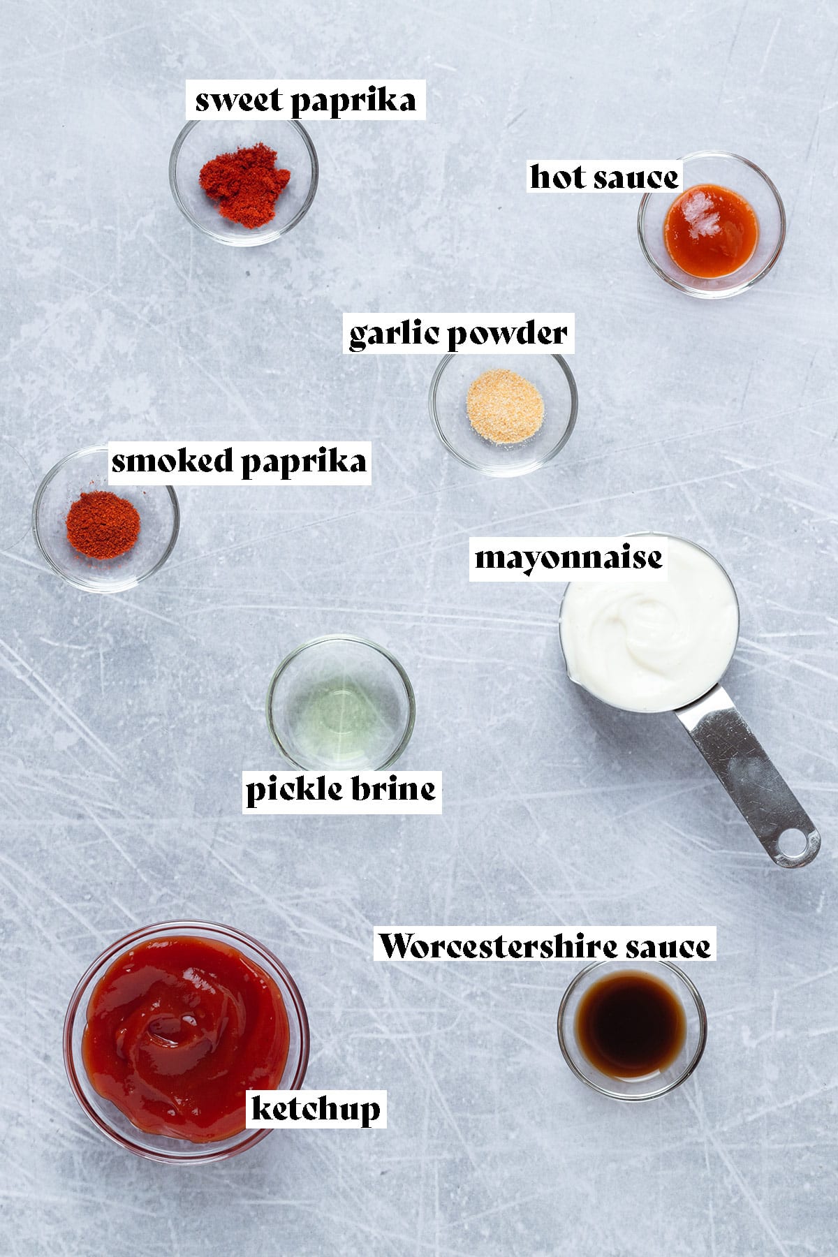 Ingredients such as ketchup, mayonnaise, and spices laid out on a grey background.