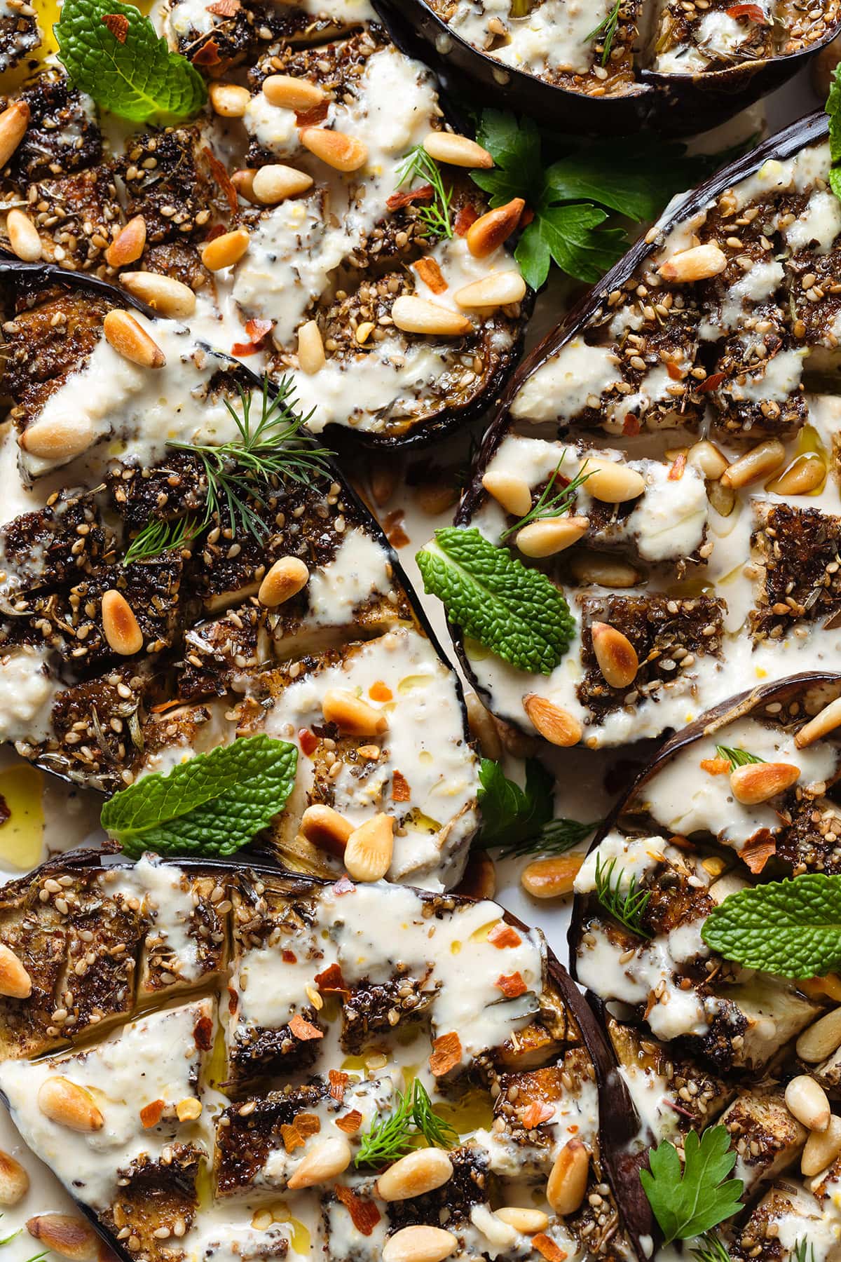 Halved roasted eggplant with spices, tahini sauce, herbs, and pine nuts.