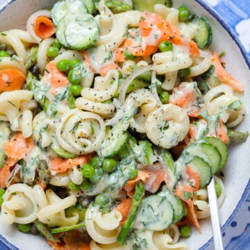 Creamy pasta salad with smoked salmon, peas, and asparagus in a white bowl on a blue tile background.