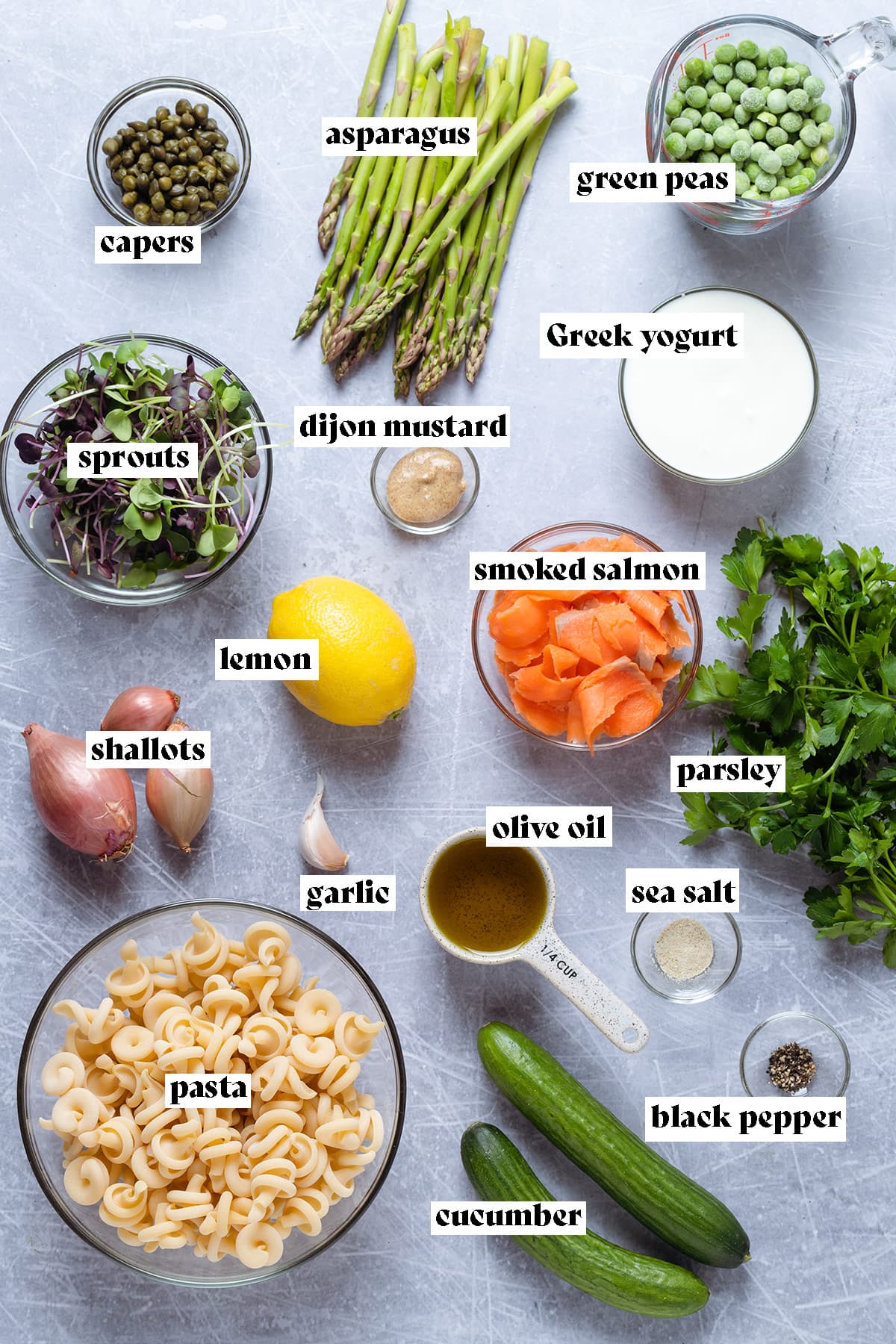 Ingredients like pasta, asparagus, peas, and smoked salmon all laid out on a grey background.
