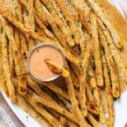 Crispy asparagus fries sprinkled with fresh parsley, served with house sauce that has one fry dipped into it.